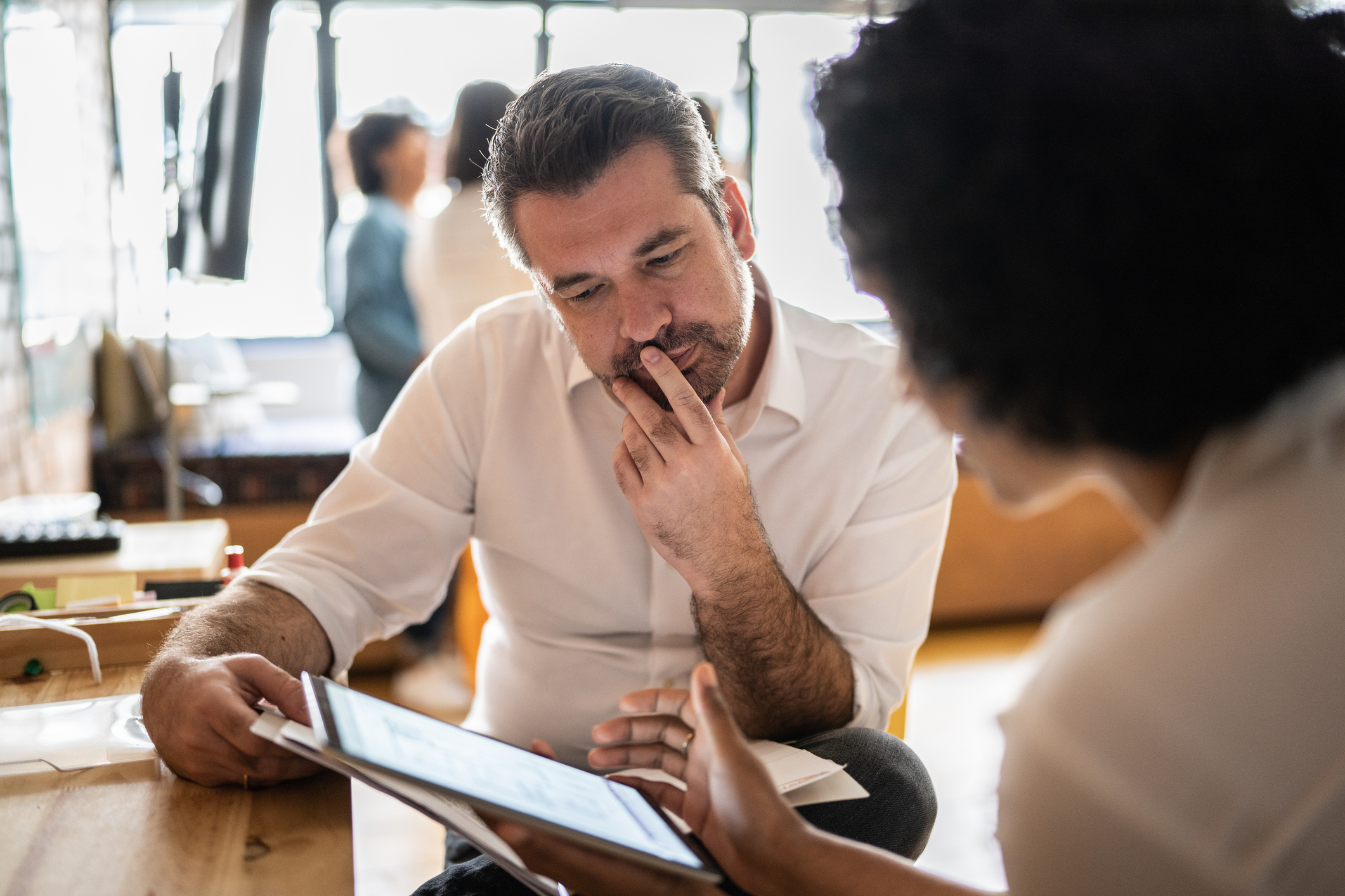 Mature man looking at a digital tablet that a colleague is showing at work Mature man looking at a digital tablet that a colleague is showing at work